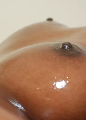 Негритянка любительница демонстрирует свое смазанное маслом тело на черном диване