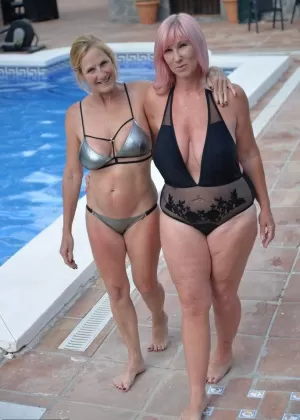 Зрелые любительницы делятся лесбийским поцелуем в своих купальниках на патио у бассейна