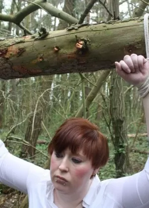 Рыжеволосая пожилая женщина щеголяет следами от веревки после того, как ее привязали к поваленному дереву в лесу