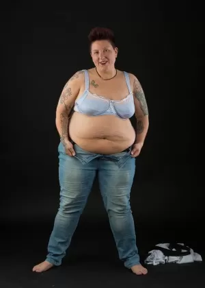 Толстая любительская татуировщица обхватывает руками свои сиськи после того, как сняла одежду