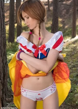 Симпатичный подросток заплетает свои рыжие волосы в косички, обнажаясь среди деревьев