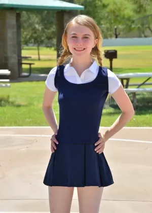 Крошечная школьница Шарлотта в униформе наклоняется за голой юбкой на улице