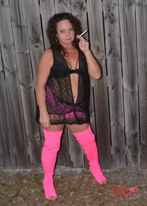 Старая любительница Дебби Делишес курит у забора в розовых сапогах до бедер